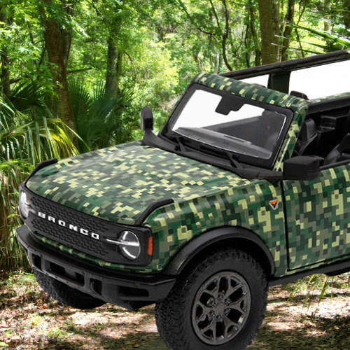 Green digital camo-wrapped Ford Bronco parked in a lush forest setting with the roof panels removed.