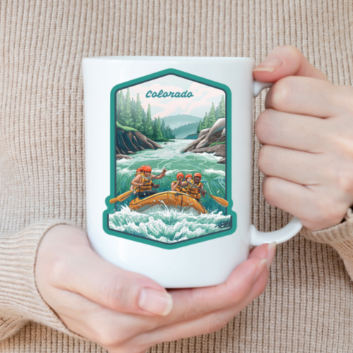 A white ceramic mug held in both hands, featuring a colorful illustration of people whitewater rafting with pine trees and mountains in the background and the word “Colorado” above.