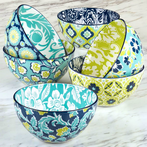 A colorful assortment of ceramic bowls featuring vibrant floral and geometric patterns in shades of blue, green, and yellow, arranged on a marble surface.