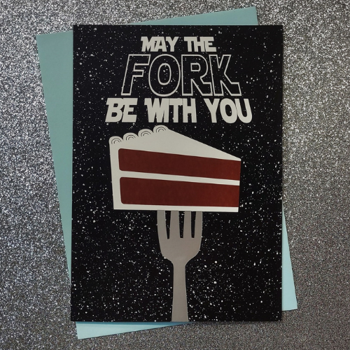 Humorous greeting card featuring a slice of cake on a fork with a starry background and bold text that reads “May the fork be with you.”