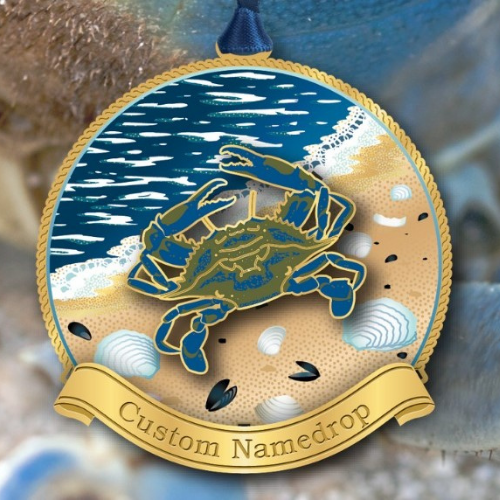 Decorative holiday ornament with an illustrated blue crab on a beach surrounded by seashells and waves, customizable with a name on the ribbon banner below.