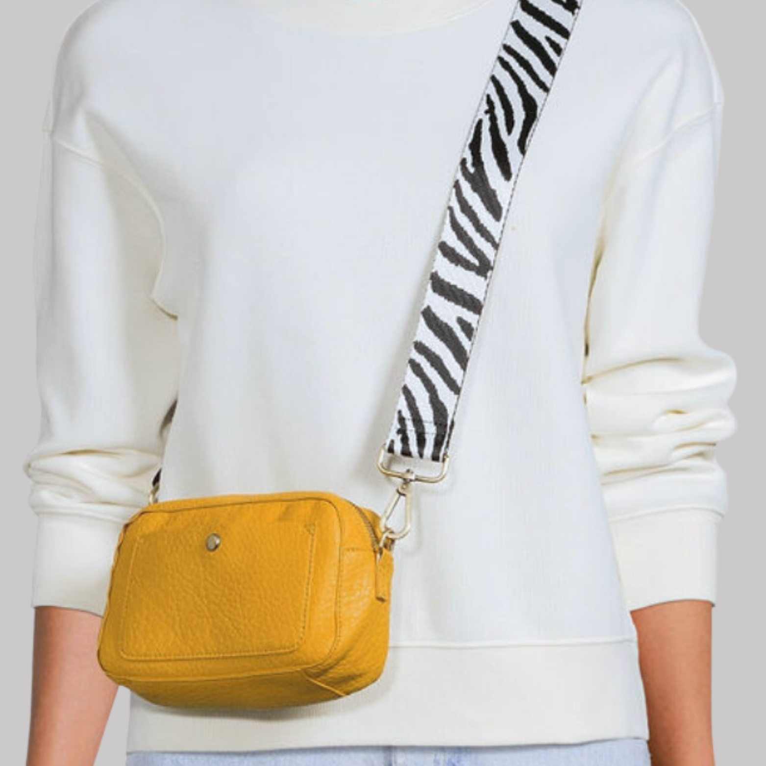 Model wearing a white sweater with a mustard yellow crossbody bag, accented with a bold black and white zebra-print shoulder strap.