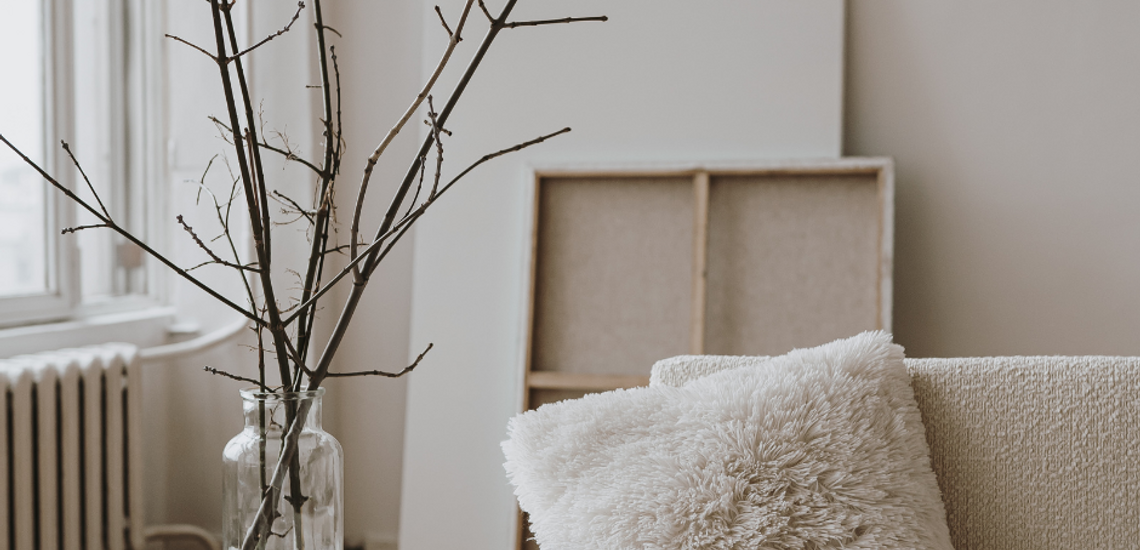 Cozy modern living space with fluffy pillow, bare branch arrangement in glass vase, and soft natural lighting.
